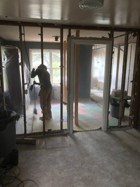 Person standing inside a partially framed room under renovation, working near a window.