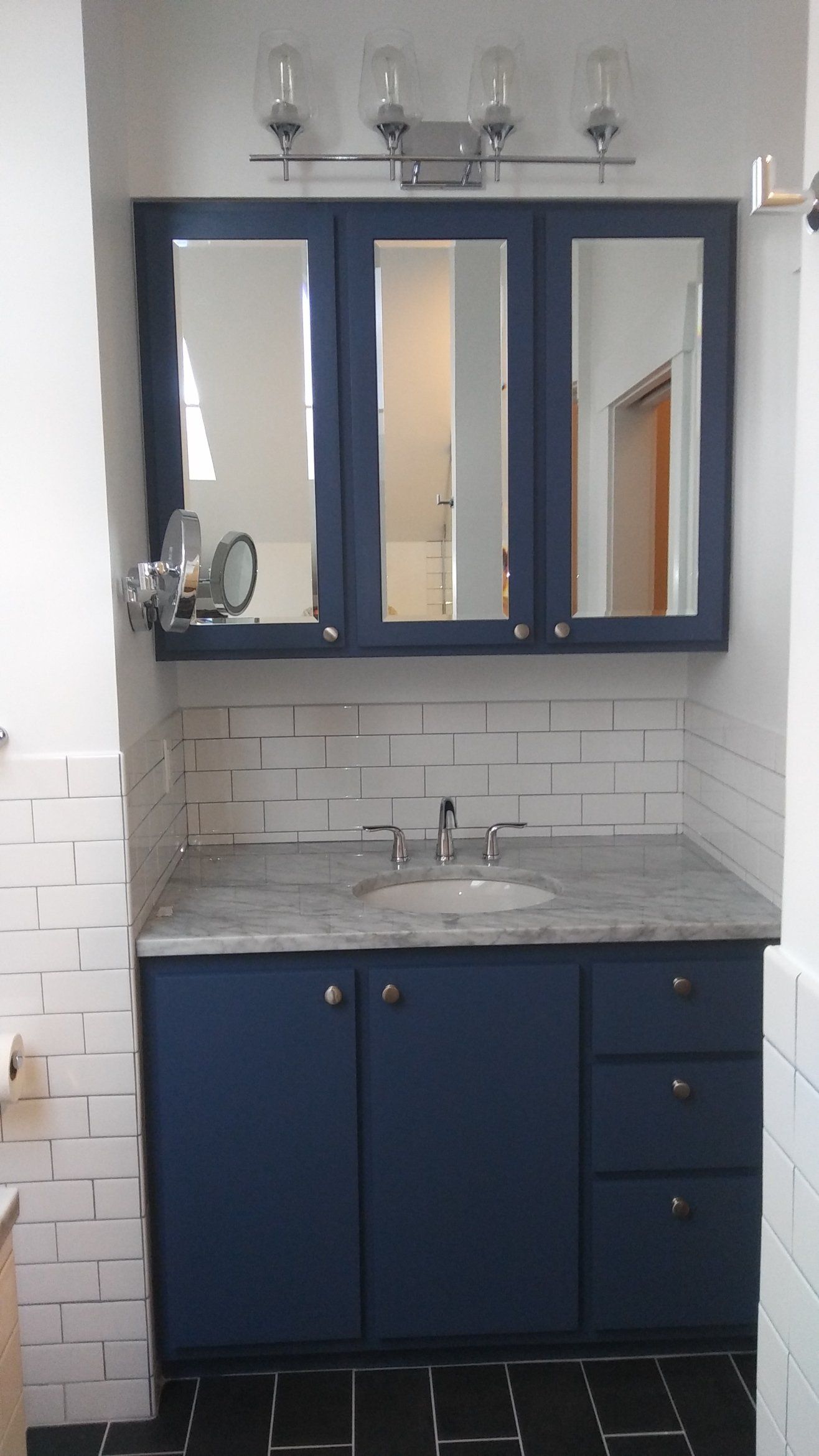 Blue bathroom vanity with mirror cabinet, sink, and wall lights against white tile.