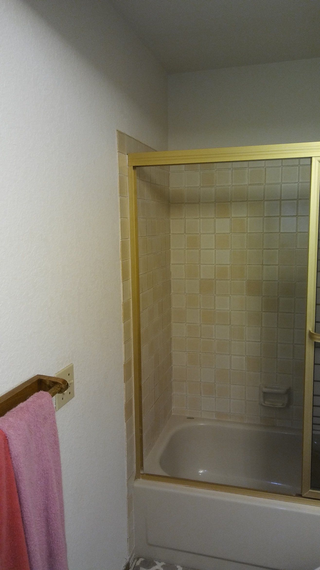 Bathroom shower with beige tile surround and a pink towel on a wall rack