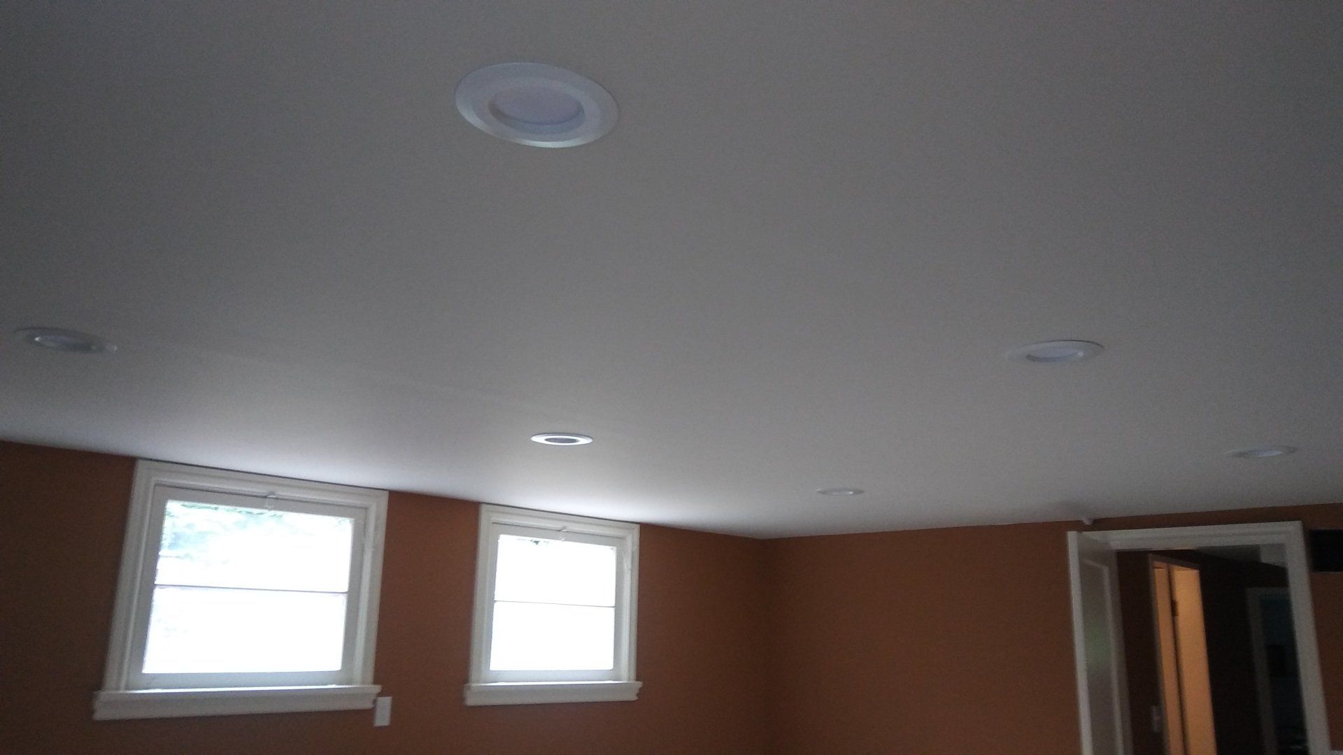 Empty room with brown walls, white ceiling, two windows, and recessed lights.