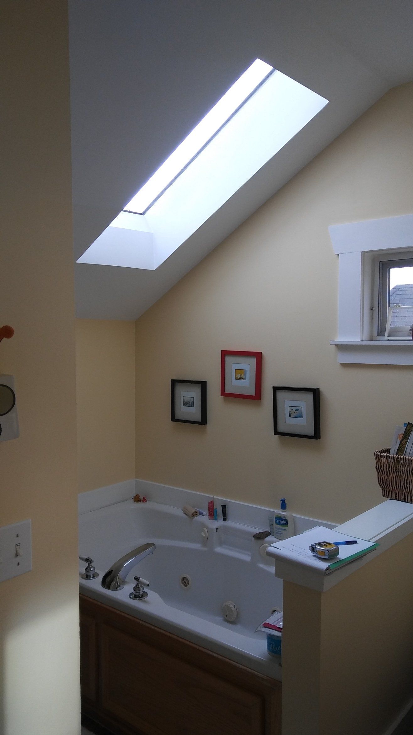 Bright bathroom with skylight, bathtub, and framed pictures on beige walls