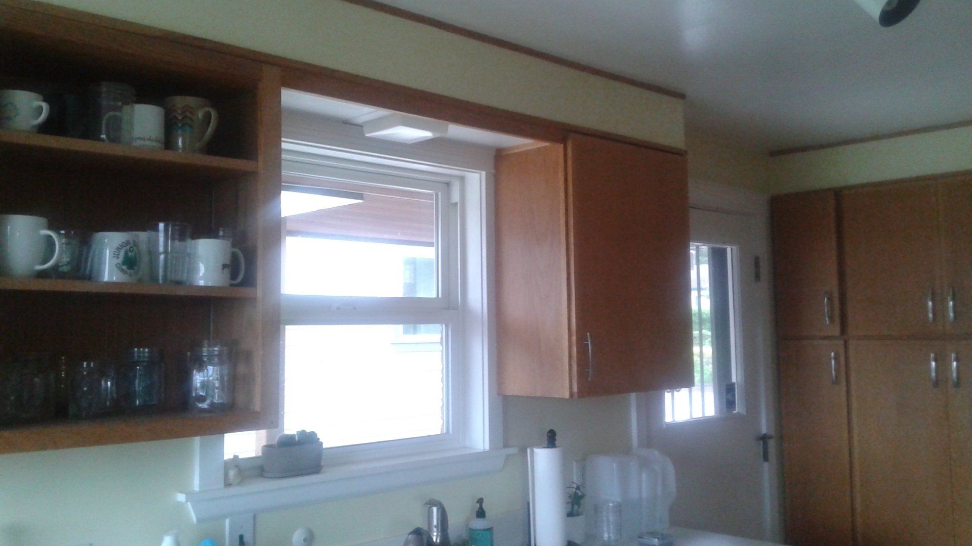 Kitchen with wooden cabinets, window above the sink, open shelves with dishes, and a countertop appliance on the right