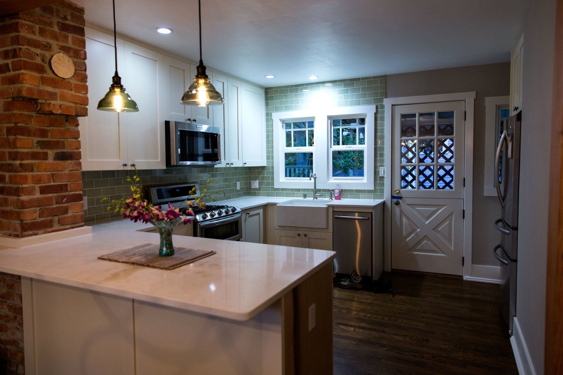 Modern kitchen with white cabinets, brick column, pendant lights, and island with flowers