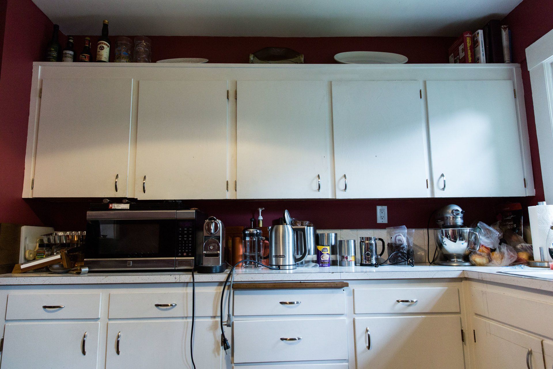White kitchen cabinets and countertop with appliances against a dark red wall.