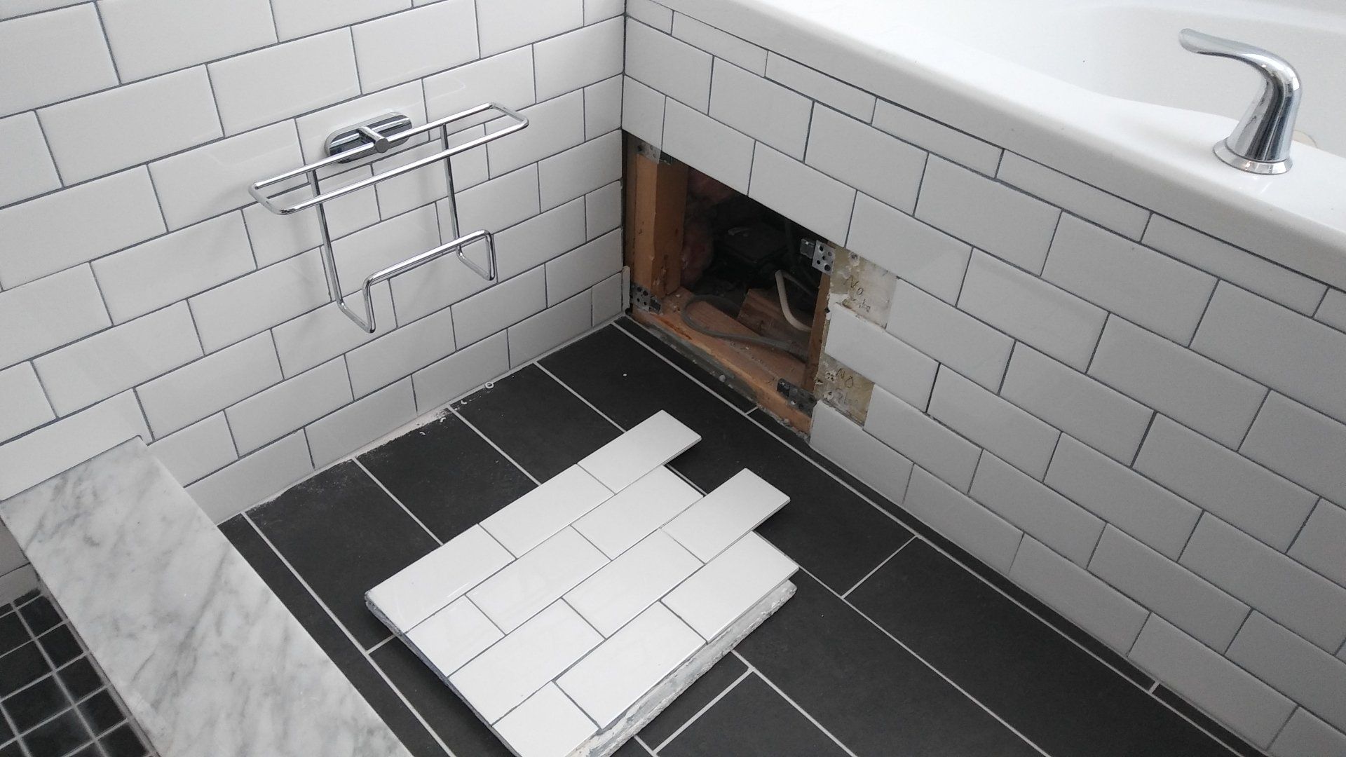 Bathroom with white subway tile, black floor tiles, and an open wall cavity under the sink.