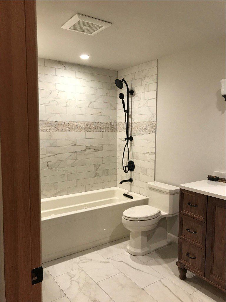Bathroom with bathtub, toilet, and wooden vanity, featuring a showerhead mounted over the tub.