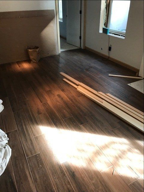 Empty room with dark wood floors, sunlight, and stacked boards near windows.
