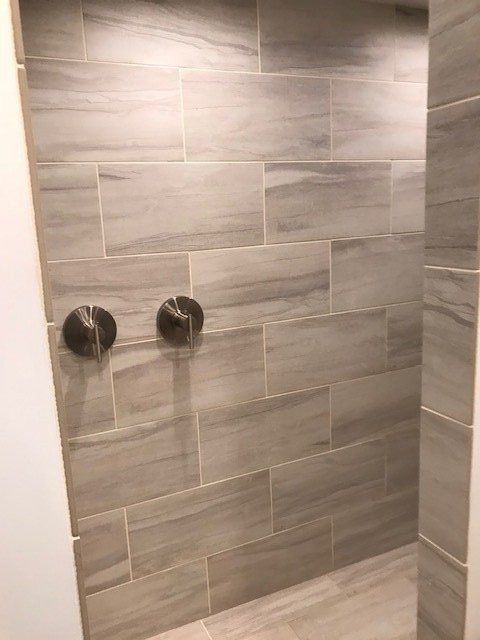 Gray-tiled shower wall with two dark circular fixtures and a small bench below