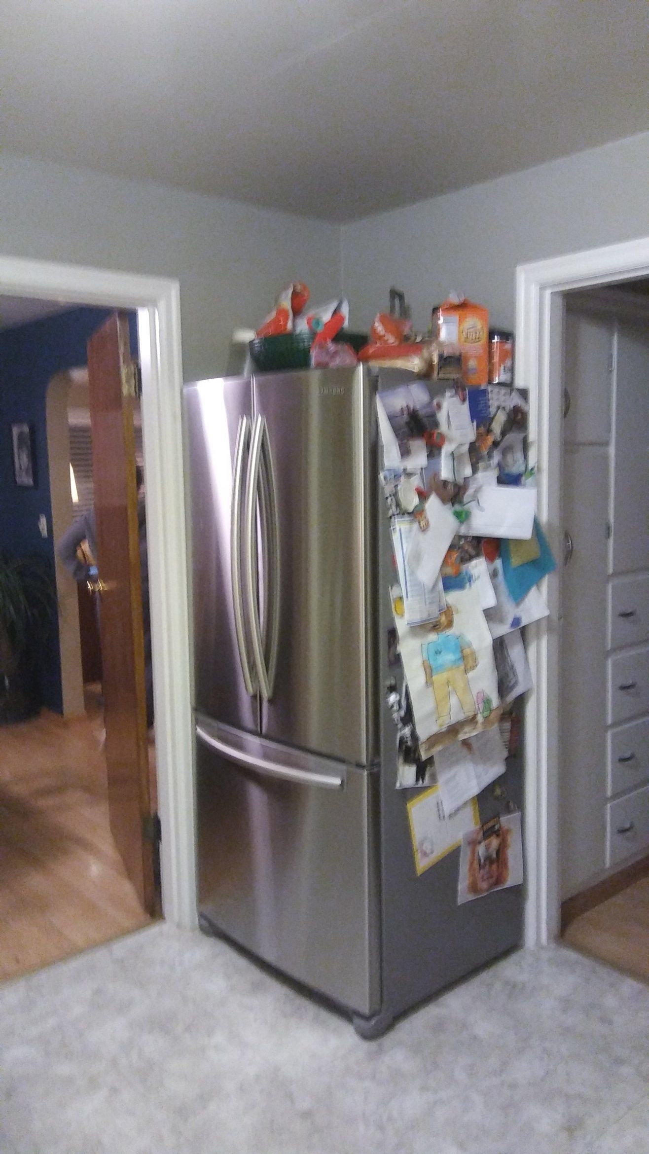 Kitchen with stainless steel refrigerator covered in notes, centered between two doorways on a carpeted floor