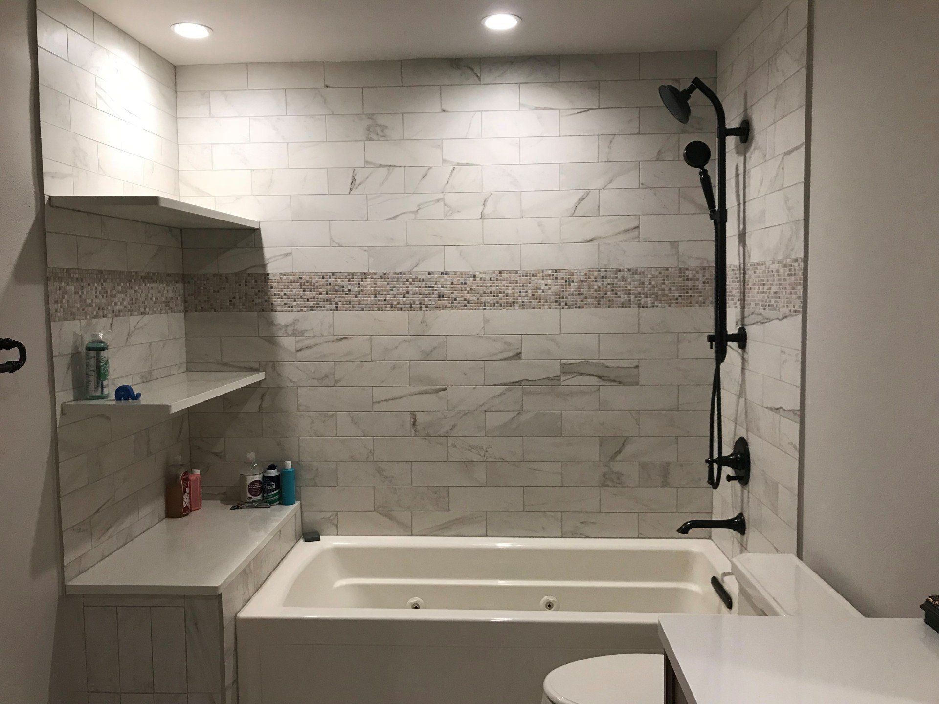 Tiled bathroom with a bathtub, built-in shelves, and a black shower head on the right.
