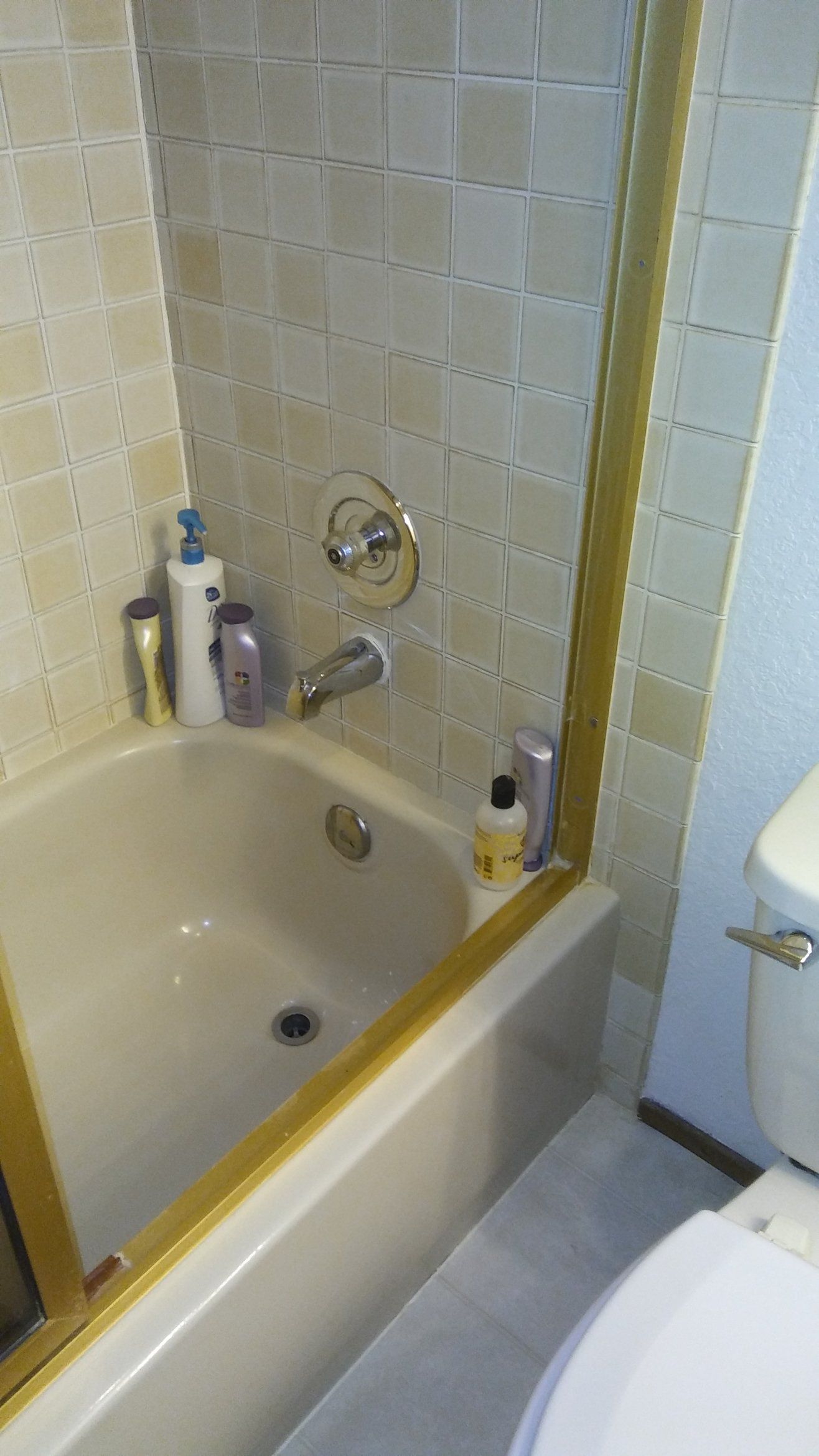 Bathtub shower area with beige tile, grab bar, soap dispenser, and toilet nearby