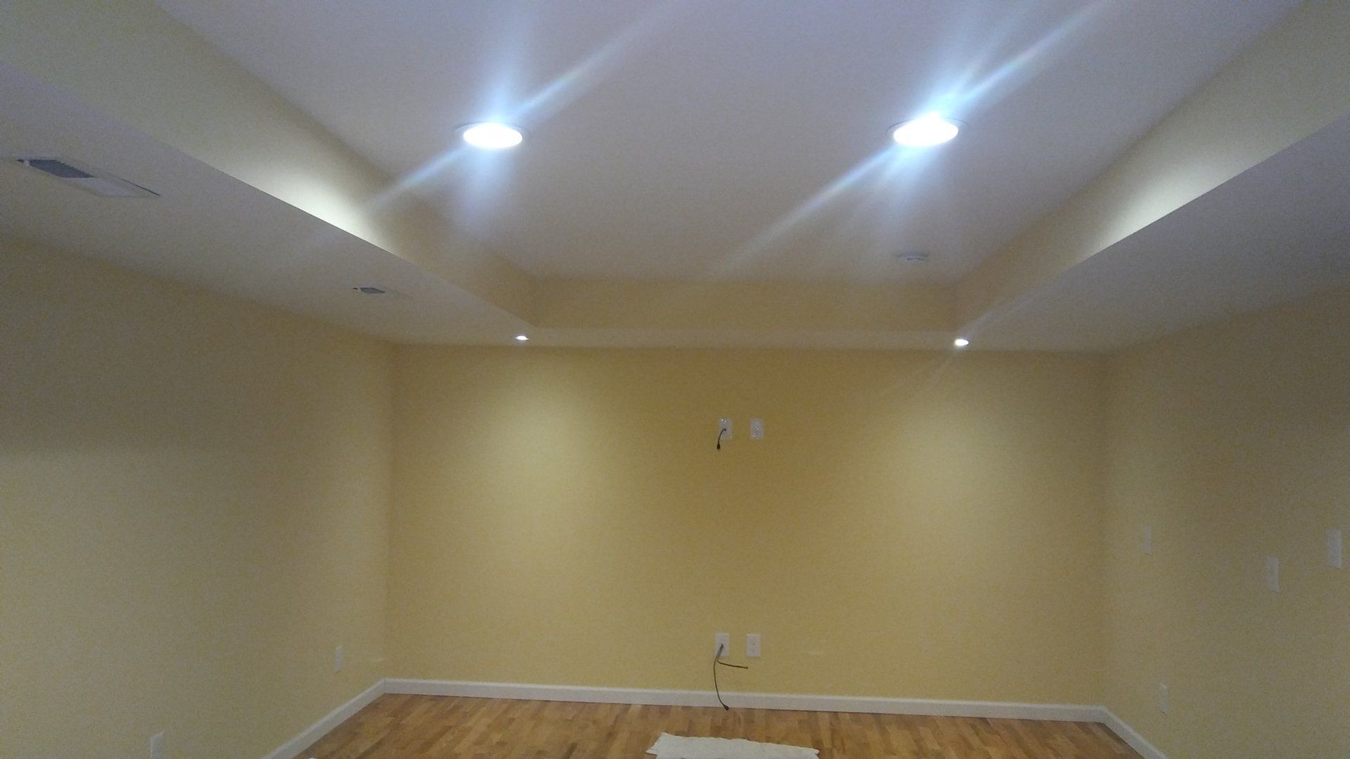 Empty beige room with recessed ceiling lights and wood trim, likely a basement or living space