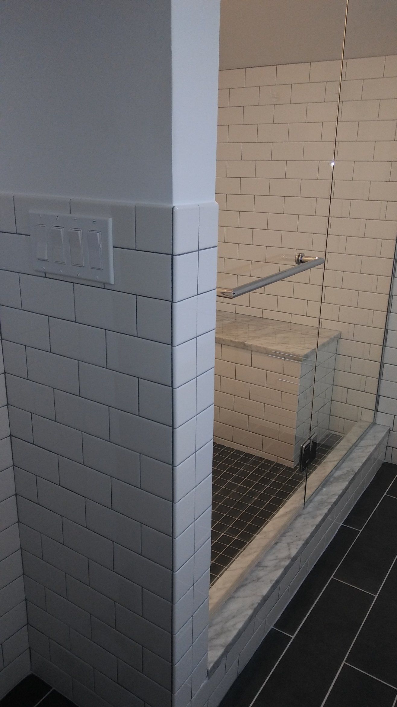 White-tiled shower stall with glass partition, bench, and dark floor tiles