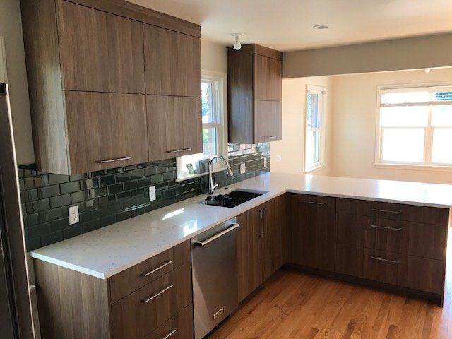 Modern kitchen with wood cabinets, white counters, dark backsplash, stainless dishwasher, and hardwood floor