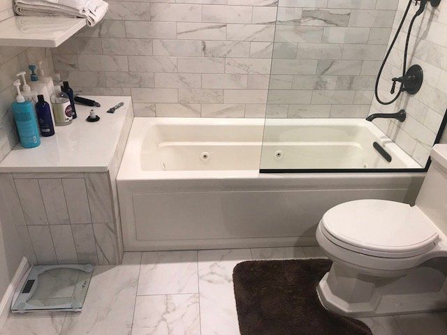 Bathroom with white tiled walls, bathtub, toilet, and sink counter with toiletries.