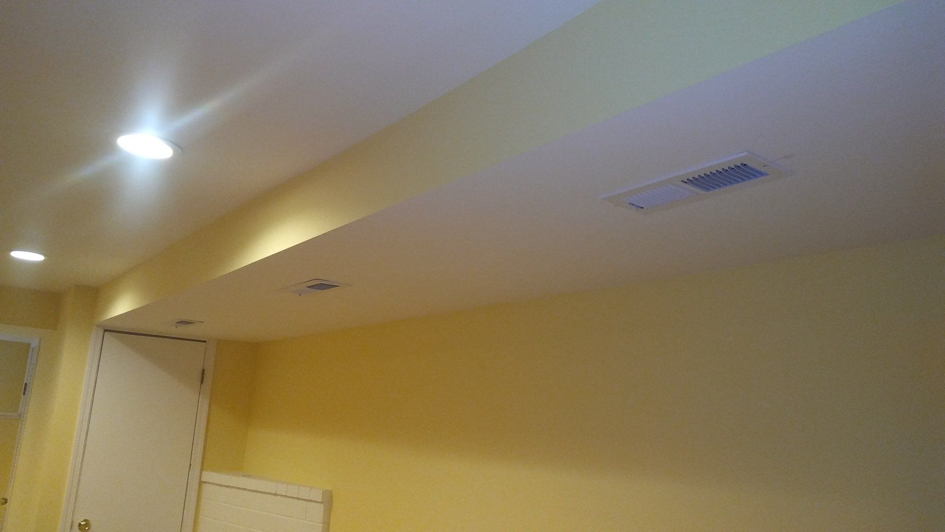 Ceiling and wall in a beige hallway with recessed lights and an air vent.