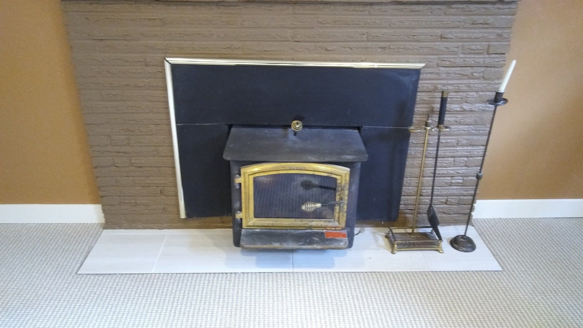 Miniature fireplace with black insert and brass trim against a brown brick wall on a white floor.