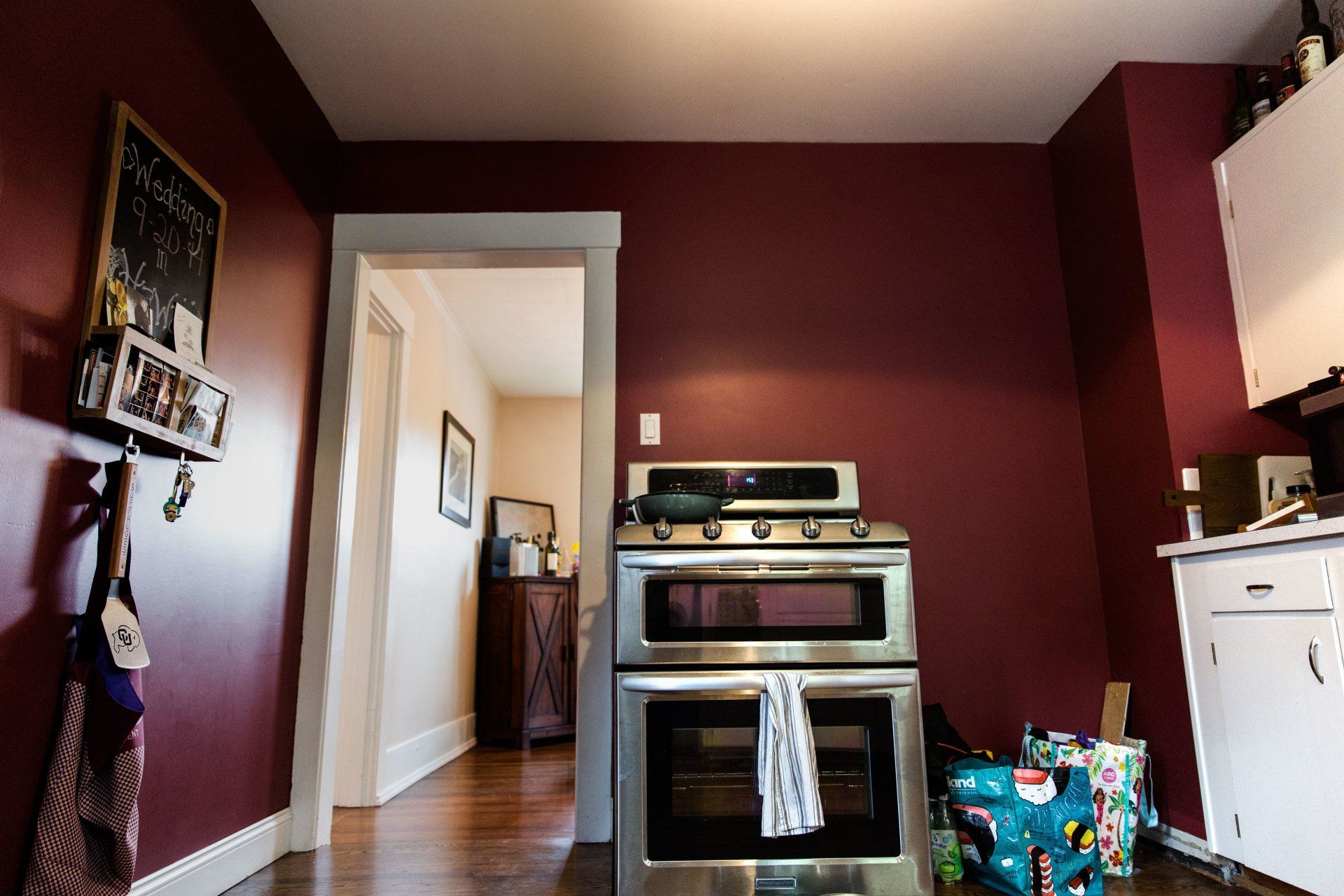 Kitchen with maroon walls, stainless steel stove, white cabinets, and a doorway to a hallway.