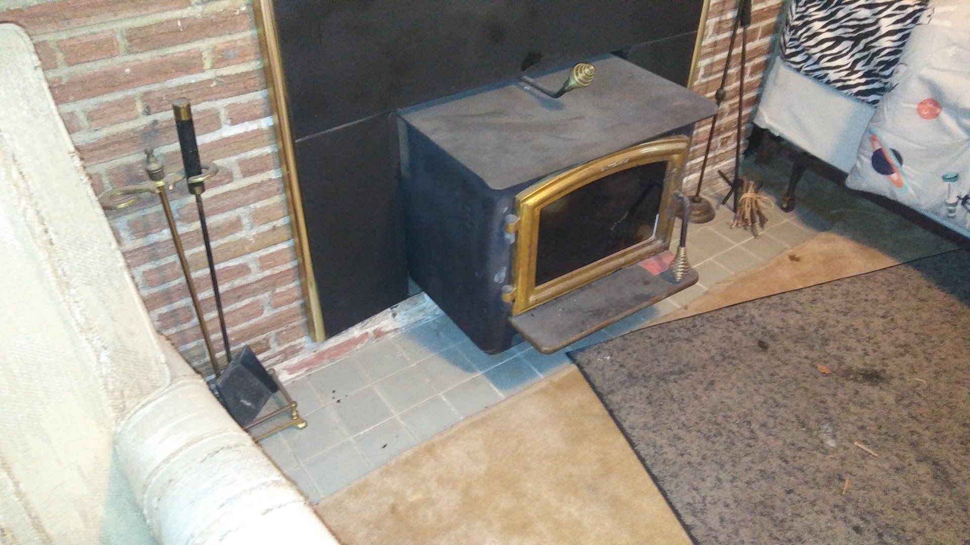 Small wood-burning stove beside a brick fireplace on a carpeted hearth area