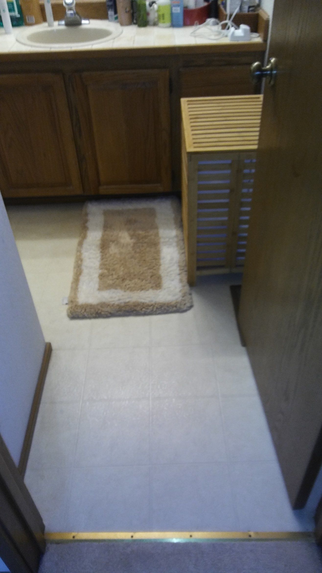 Narrow doorway into a kitchen with tiled floor, sink cabinets, and a small rug by the counter.