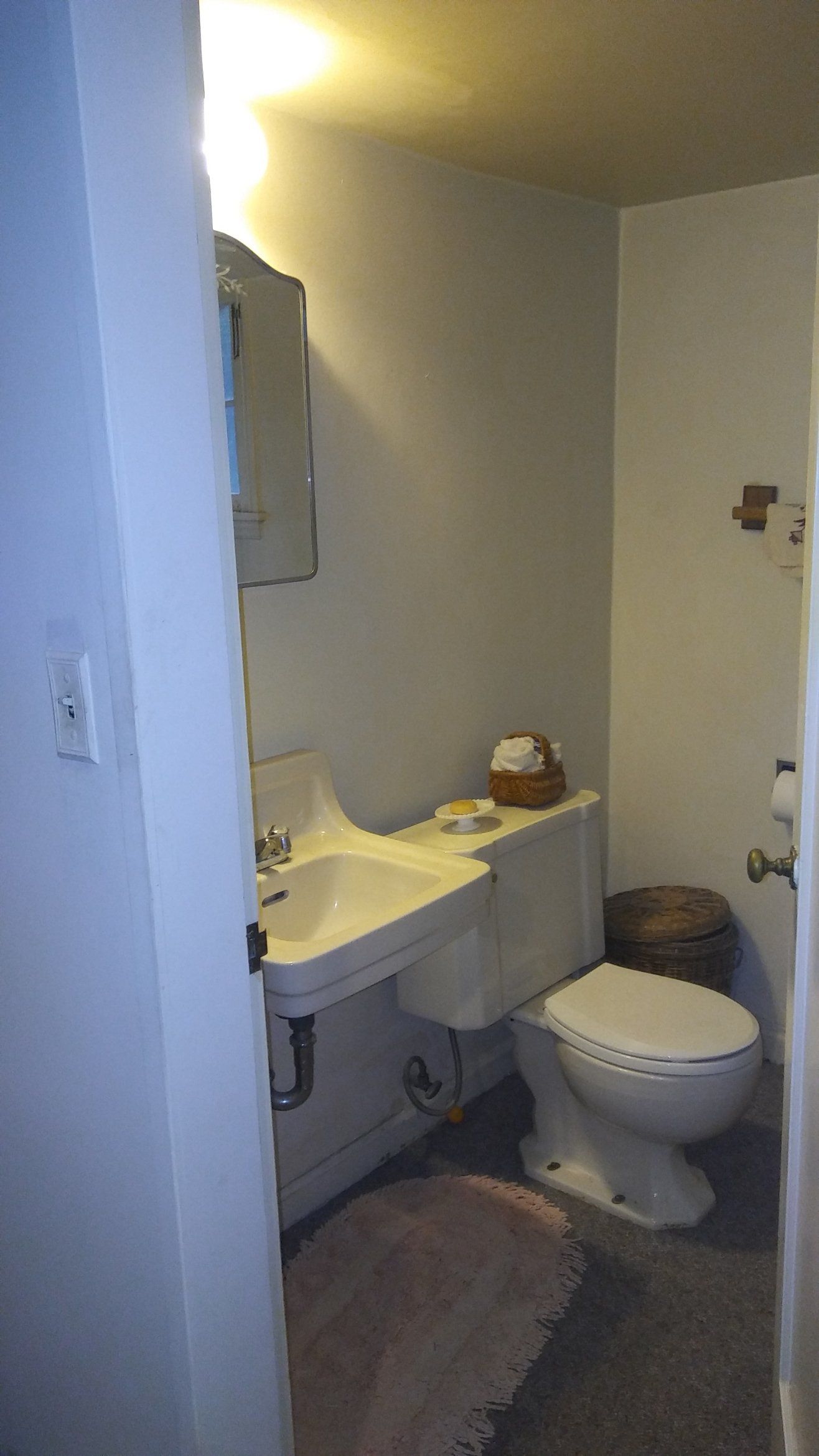Small bathroom with a sink, toilet, bathtub, and tan rugs, viewed through a doorway.