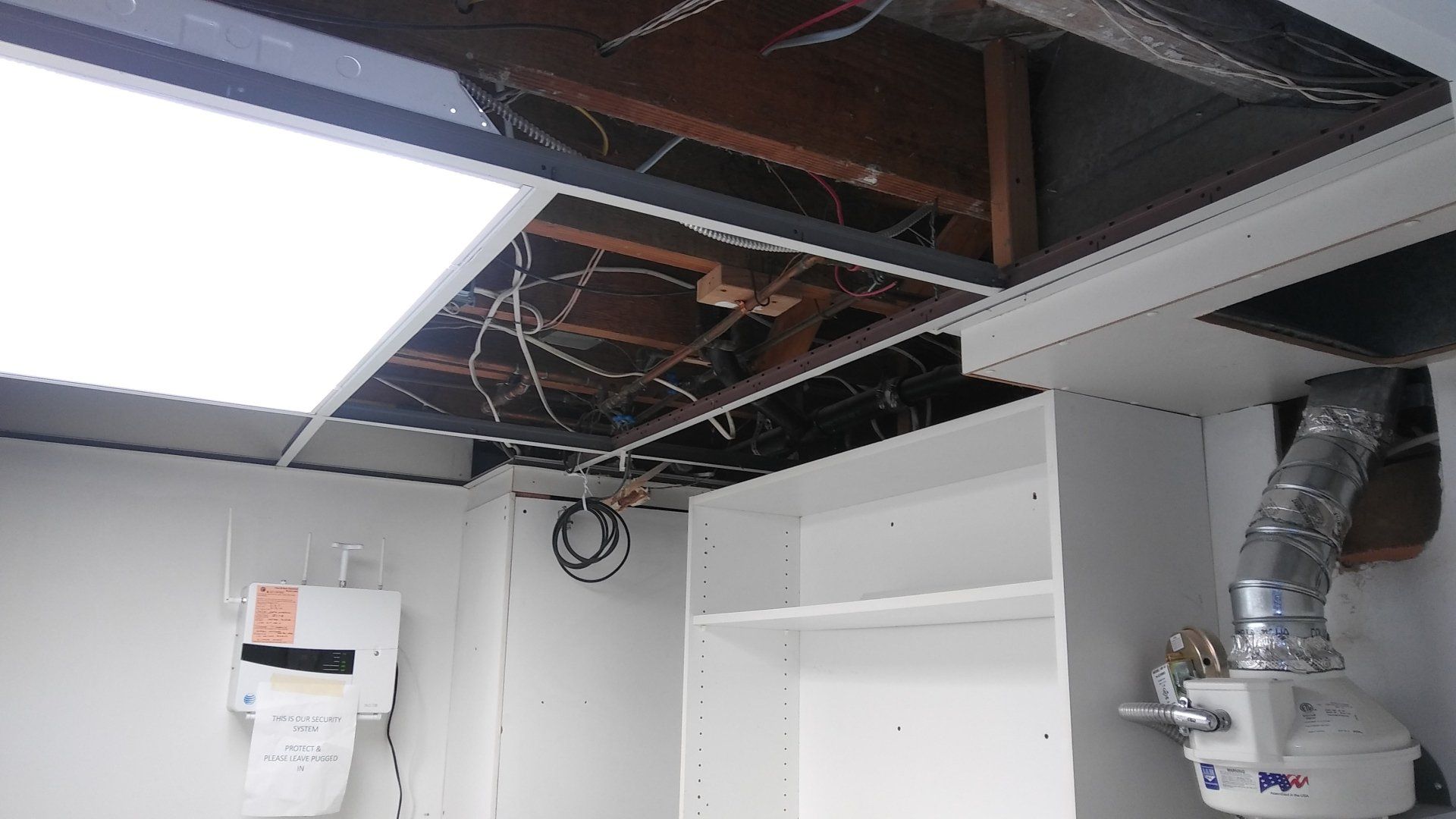 Exposed ceiling with wiring and ductwork above a partially unfinished white room.