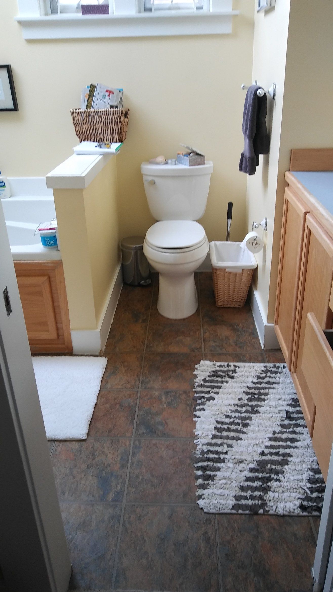 Small bathroom with a toilet, wicker trash bin, towel, wood vanity, and patterned rugs.