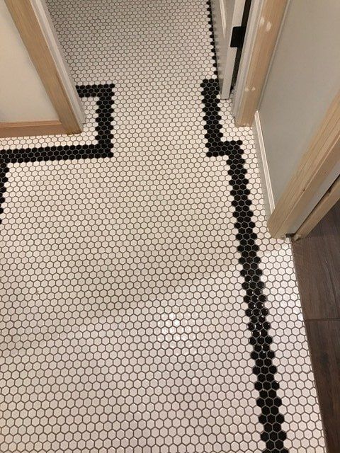 Narrow hallway with white hex tile floor and black border trim between open doors