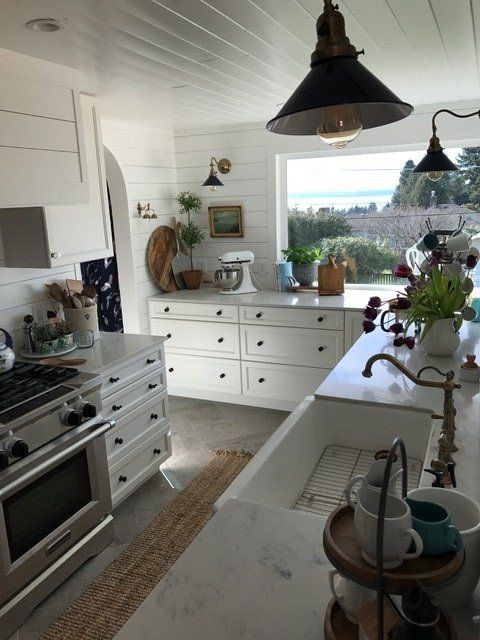 Bright white kitchen with marble island, black pendant lights, and a window view of the sea