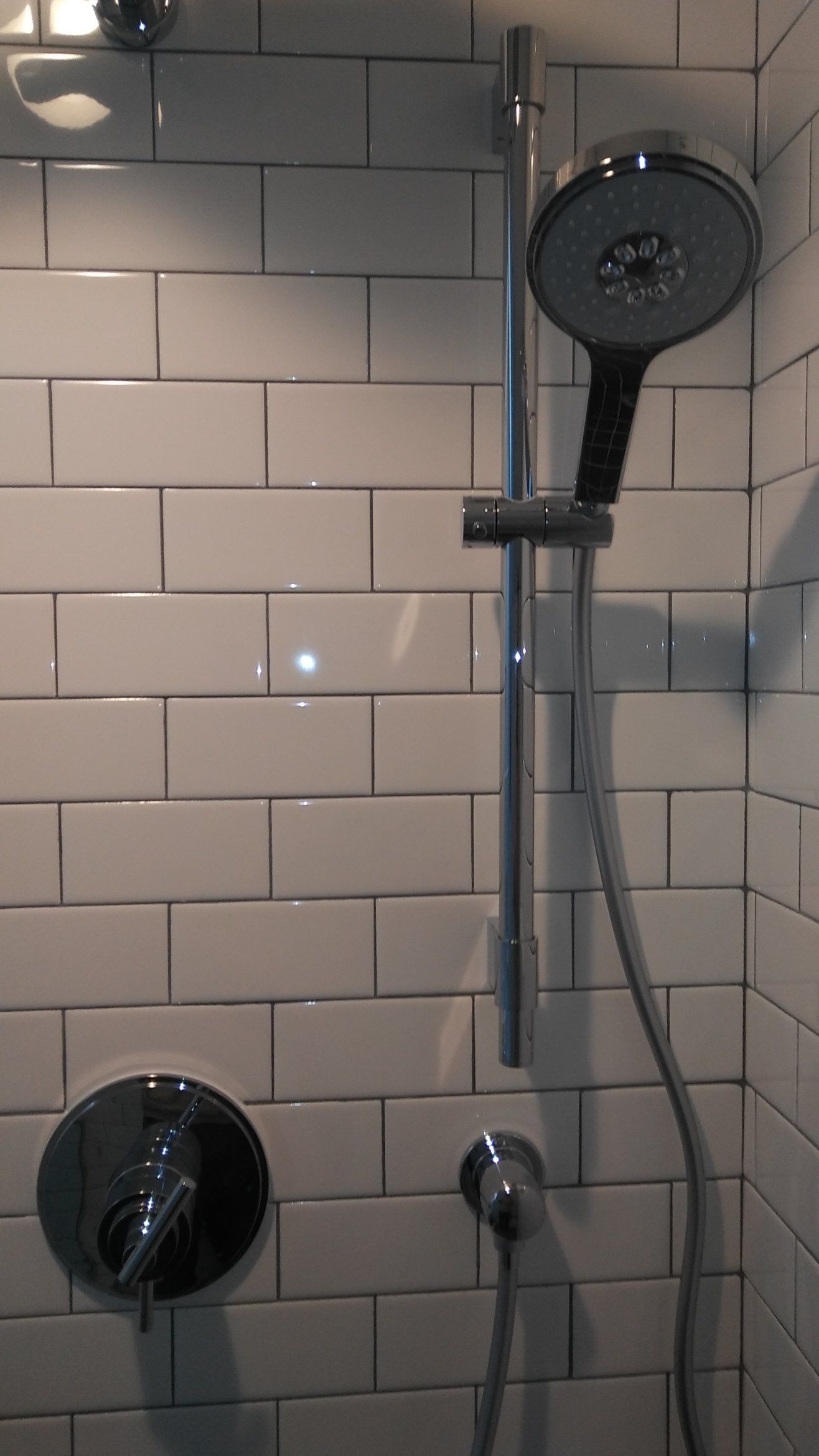 Tiled shower with chrome showerhead, handheld sprayer, and fixtures against white subway tiles.