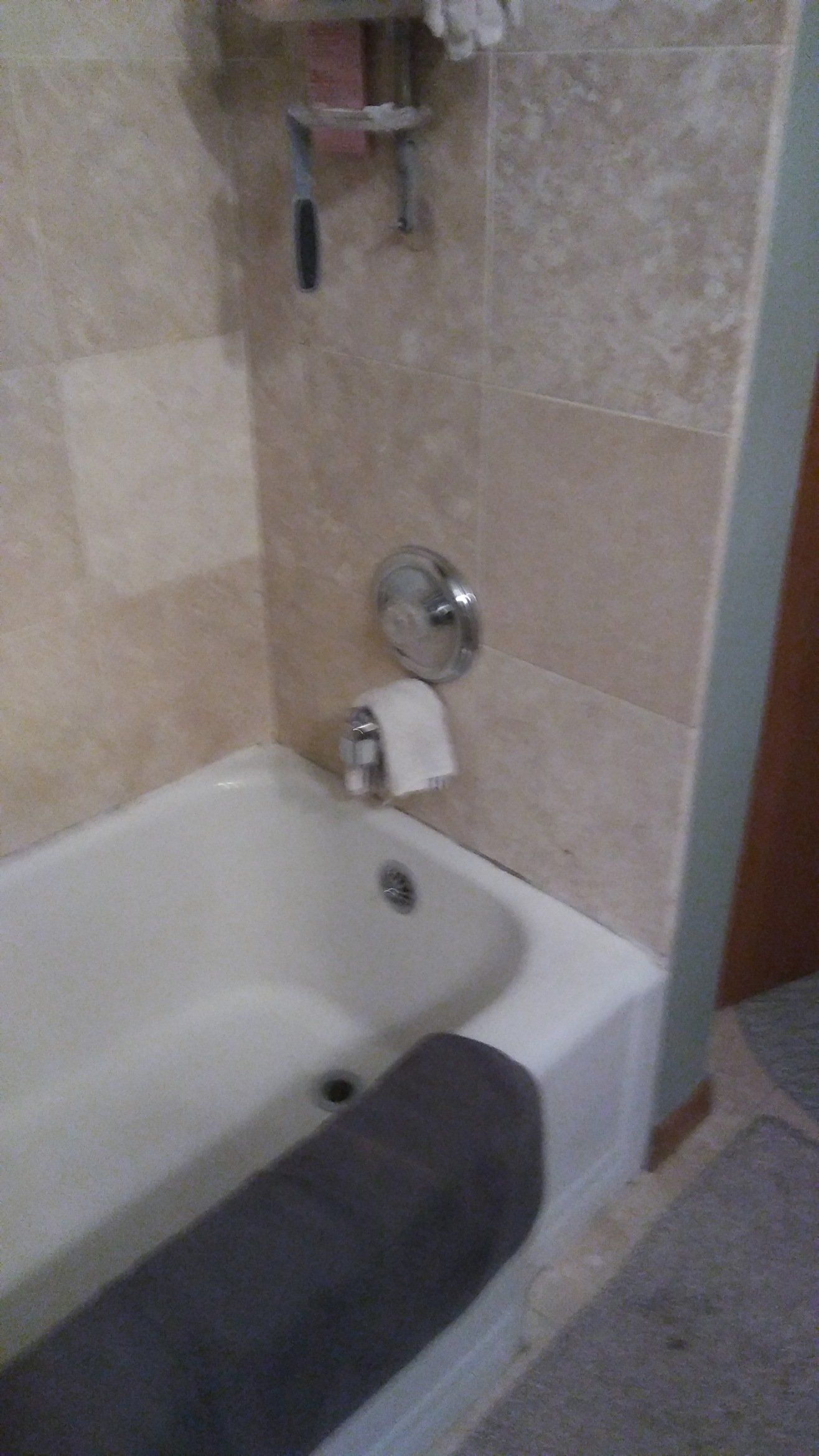 Bathroom tub with beige tile walls, chrome fixtures, and a dark gray towel draped over the edge