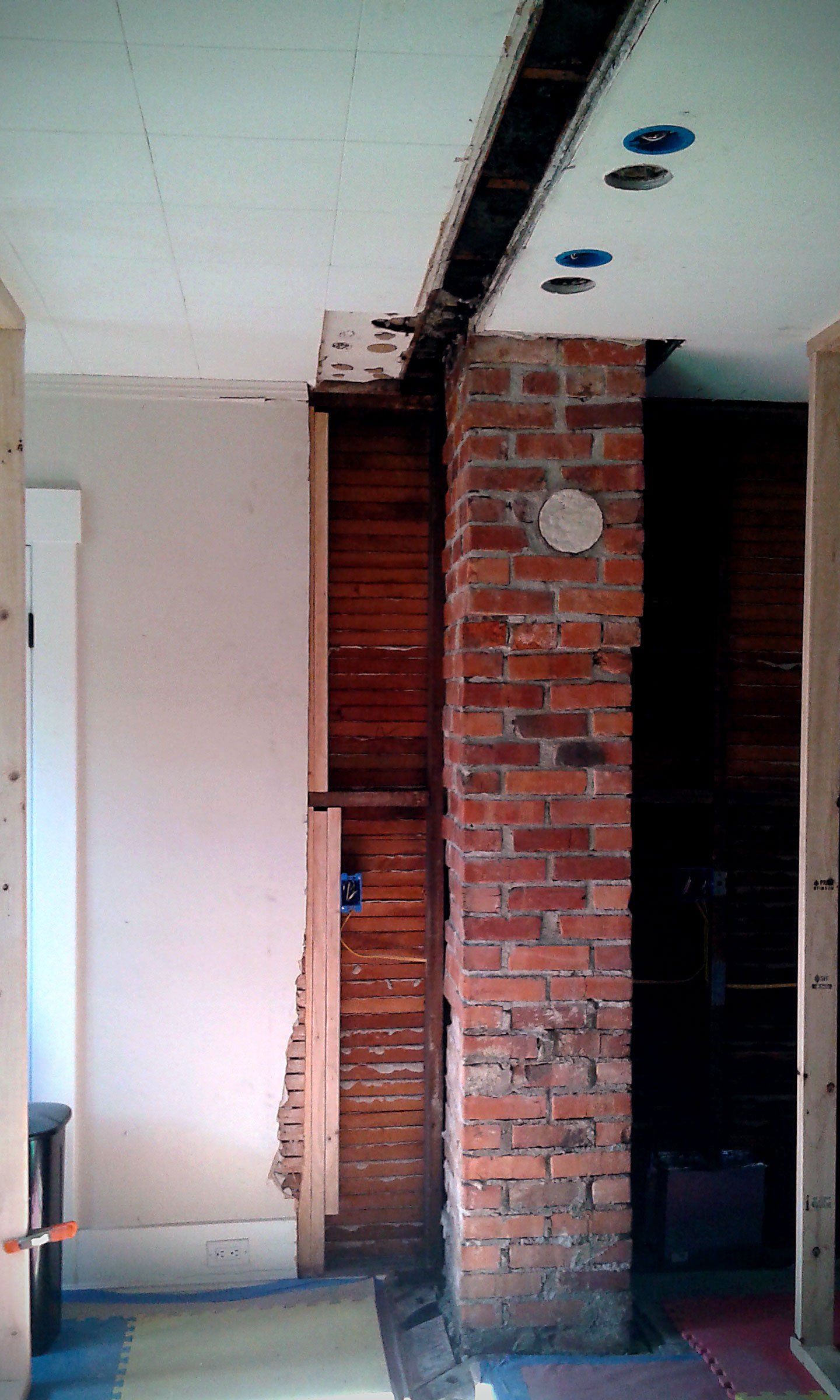 Partially renovated room with exposed brick column, white walls, and ceiling recesses