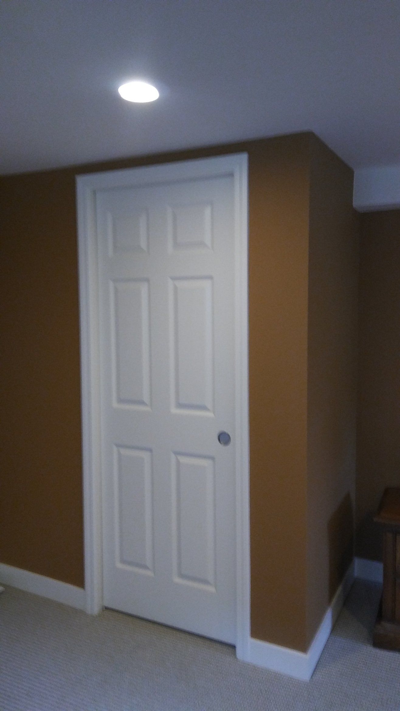 White paneled door in a tan hallway corner with a ceiling light above.