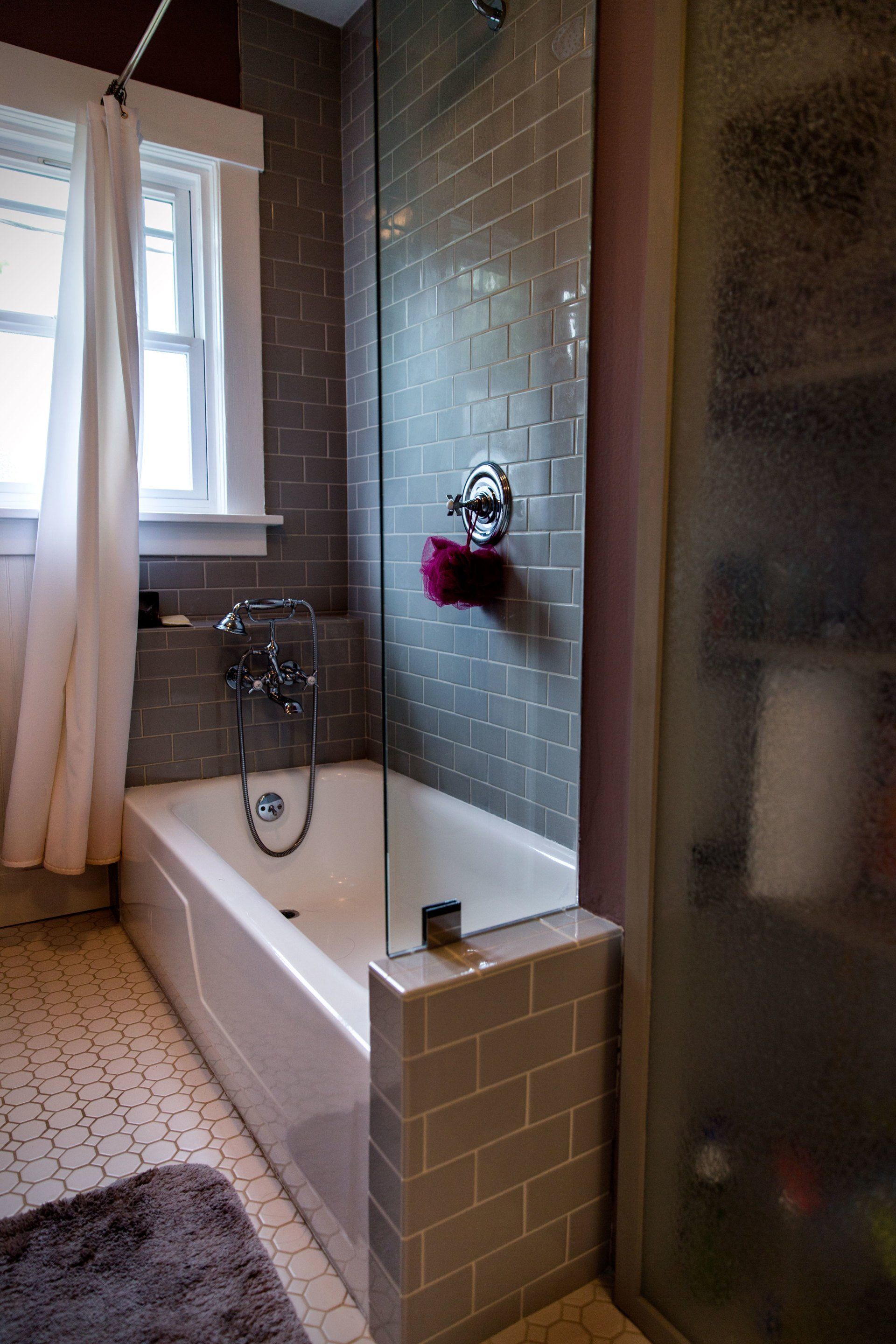 Small bathroom with a white tub, gray tile, shower curtain, and frosted glass shower enclosure.