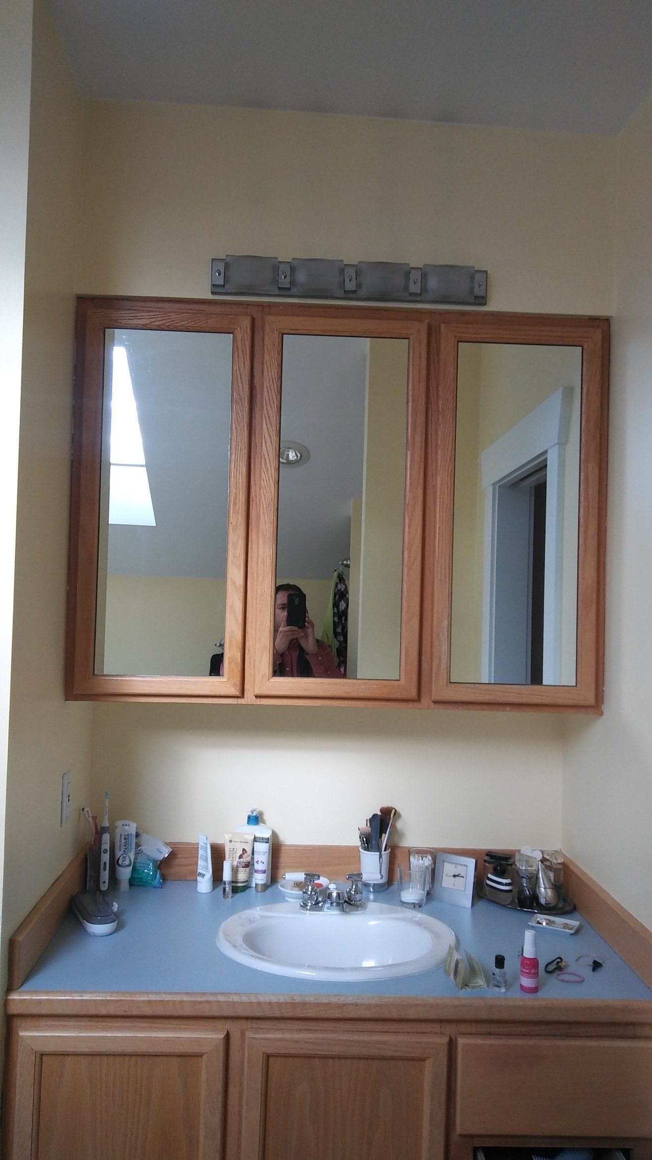 Bathroom vanity with wooden mirror cabinet, white sink, and toiletries on a light blue countertop.