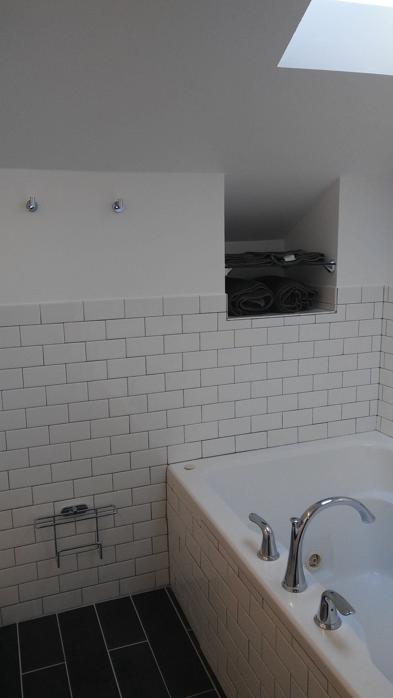 Small bathroom with white tiled wall, bathtub, sink, and a skylight above.