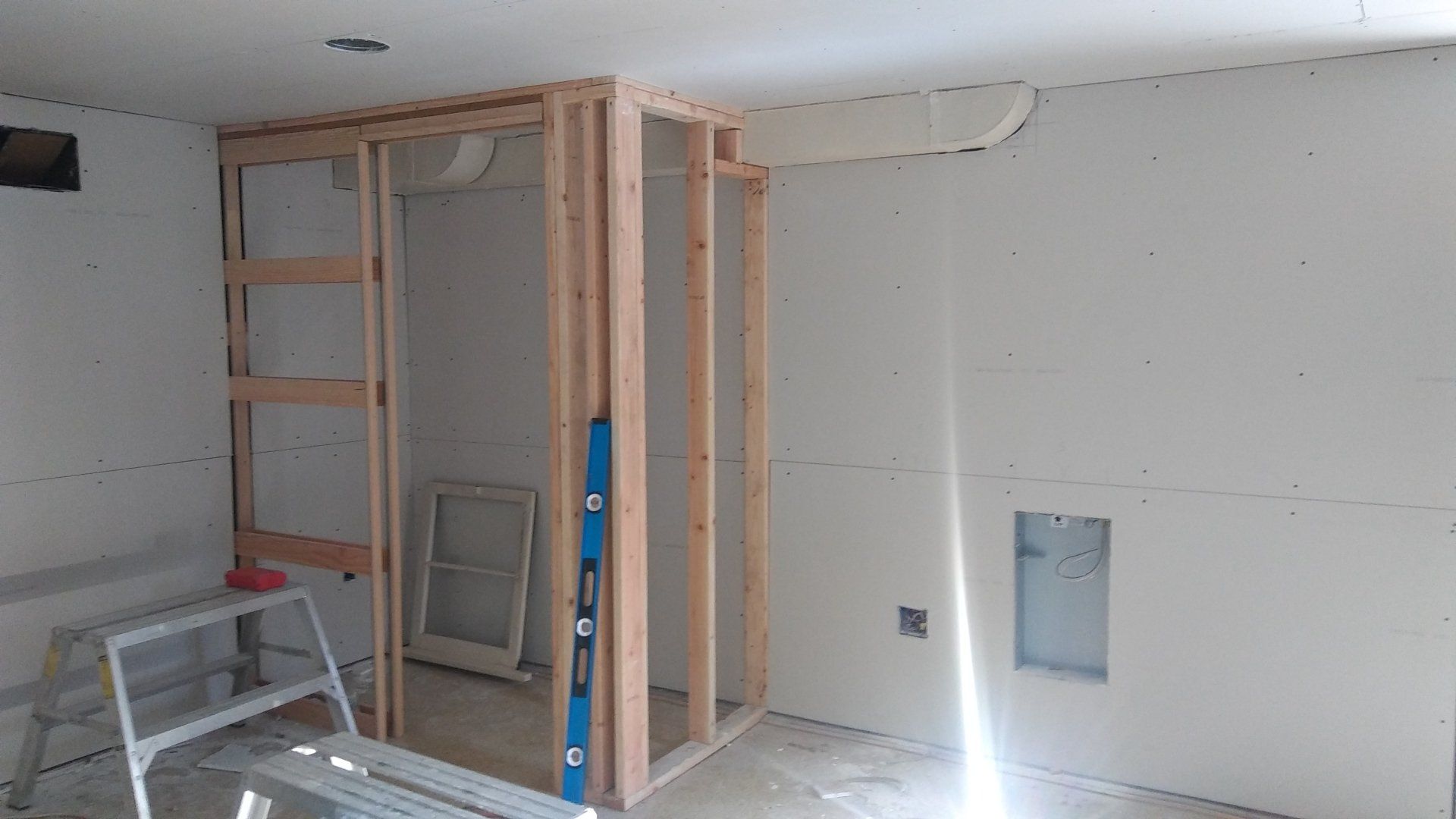 Partially framed room under renovation with drywall, a ladder, and construction tools on the floor