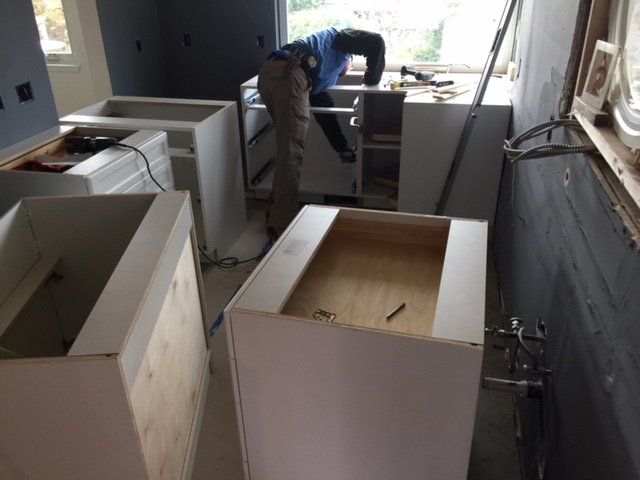 Partially renovated kitchen with unfinished white cabinets and a worker near the back wall