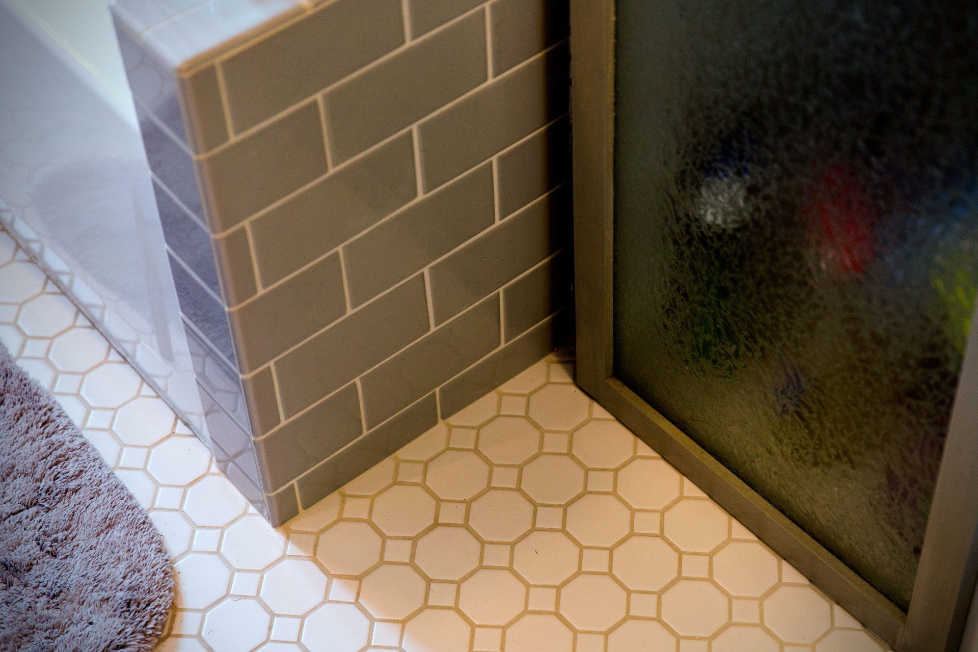 Bathroom corner with gray tiled wall, white hexagonal floor tile, and frosted glass shower door