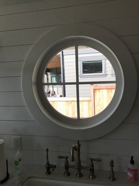 Round window above kitchen sink with faucet and soap dispenser, looking out to a patio and fence