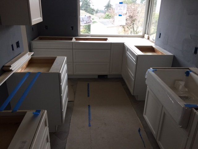 Unfinished kitchen with white cabinets, open window, and blue painter’s tape marking the floor.