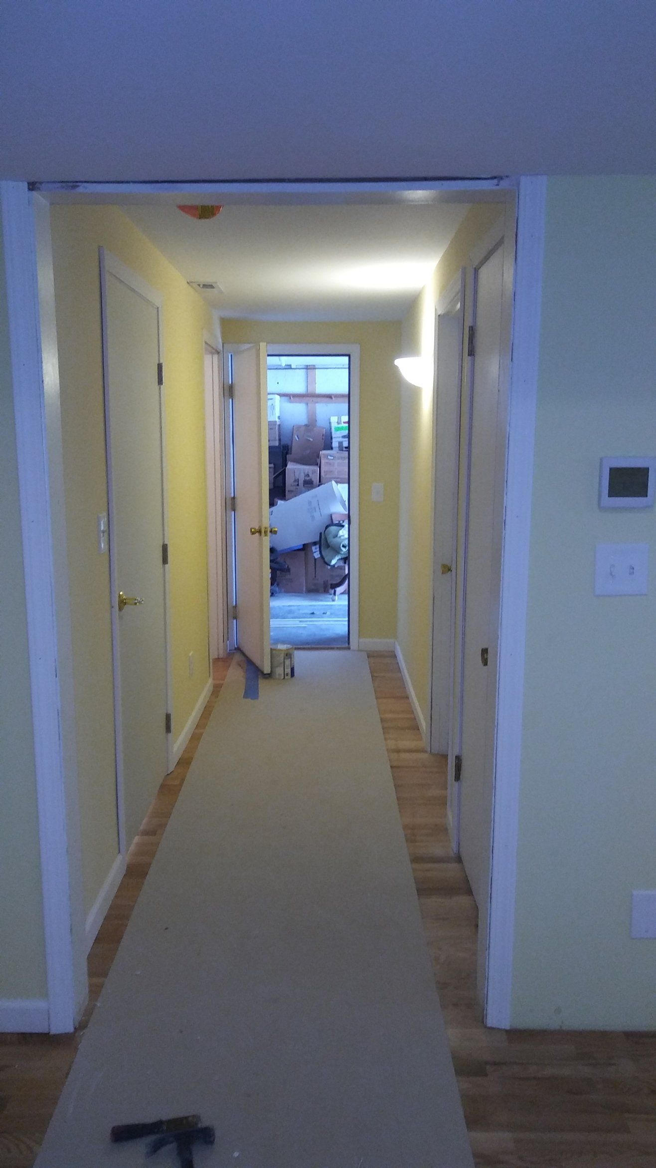 Narrow hallway with beige carpet, white walls, and an open front door at the far end.