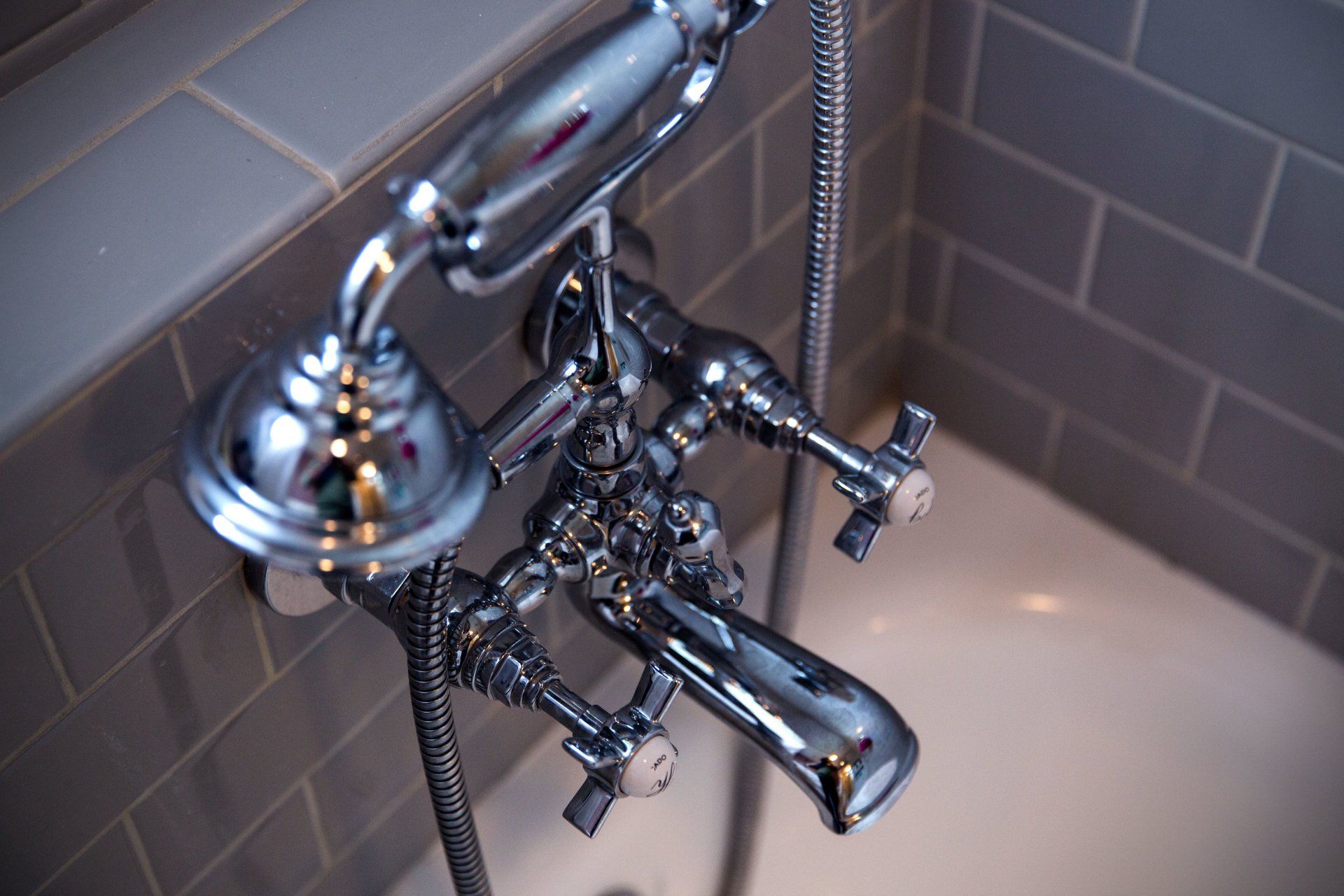 Chrome vintage bathtub faucet with handheld showerhead against tiled bathroom wall