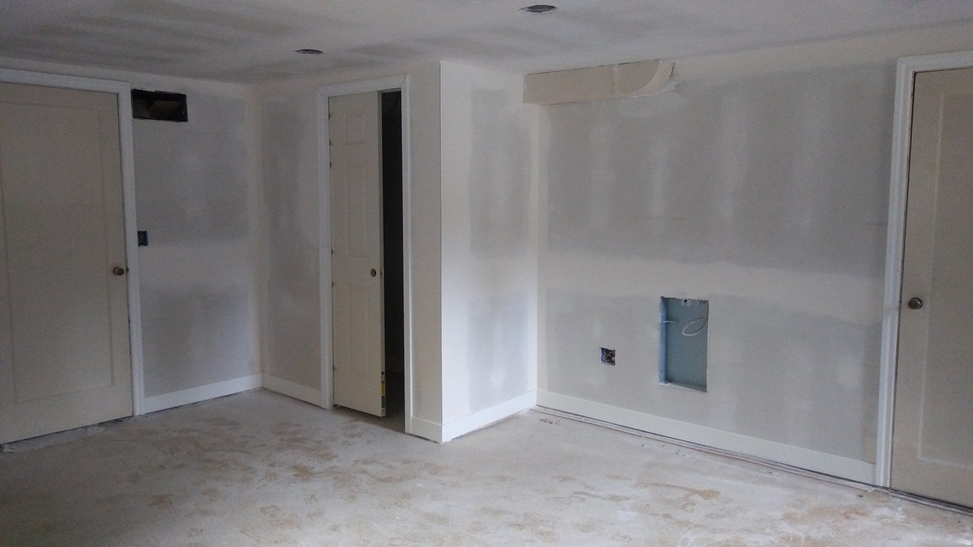 Empty unfinished room with white drywall, doors, and bare floor during renovation