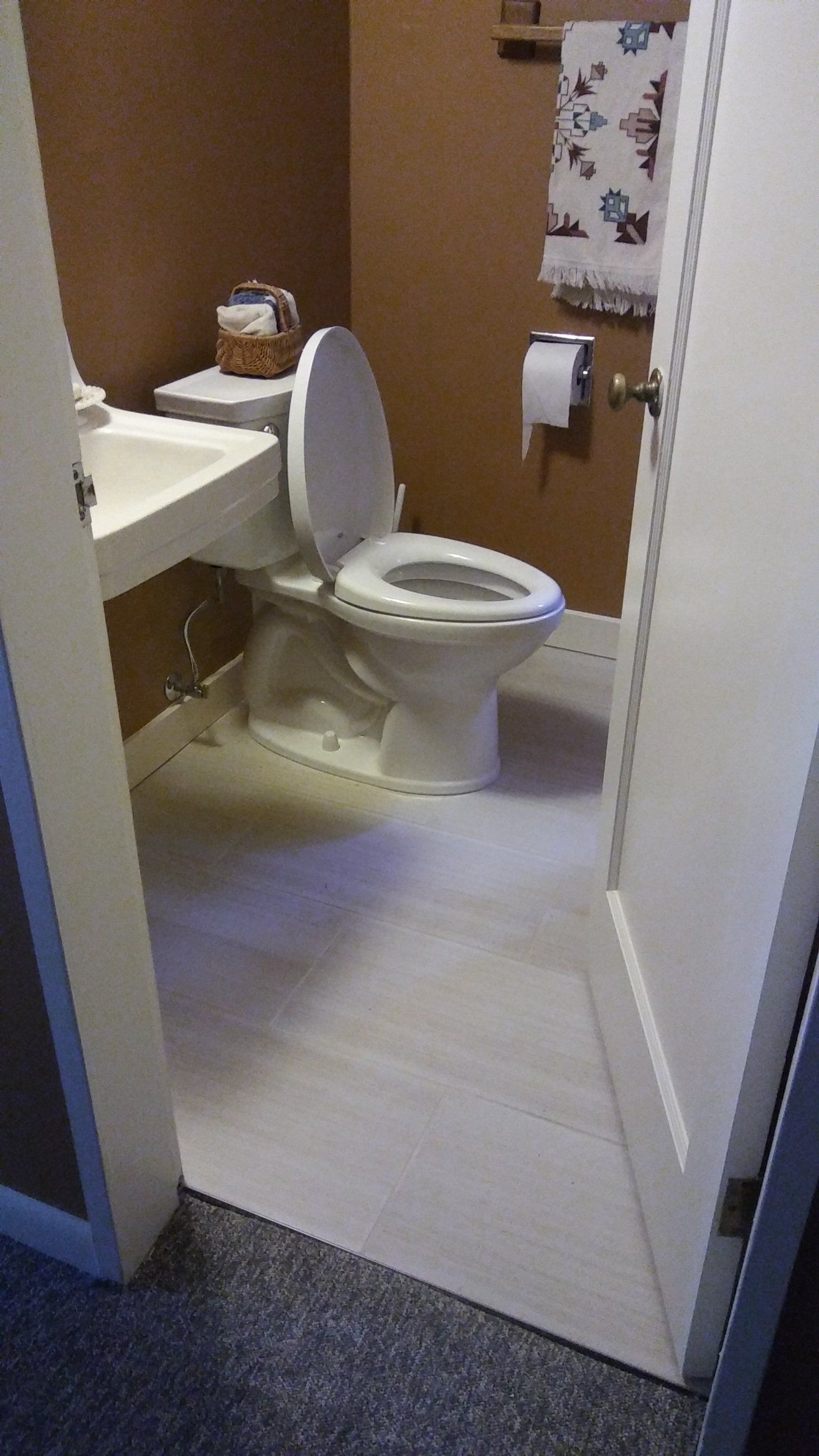 Small bathroom with a white toilet, sink, and tiled floor viewed through a doorway.