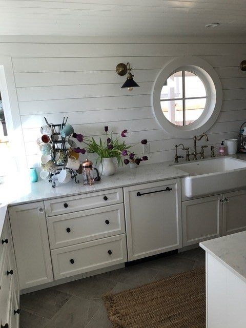 White farmhouse kitchen with sink, round window, and countertop decor