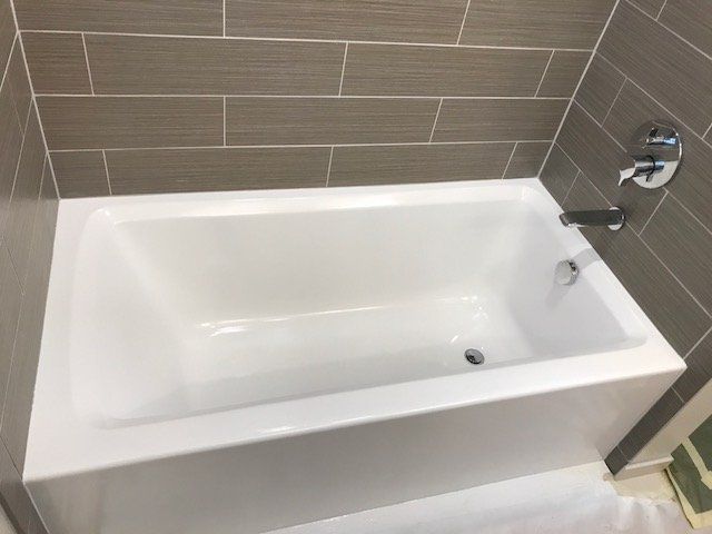 White bathtub in a tiled bathroom with chrome faucet and beige wall tiles