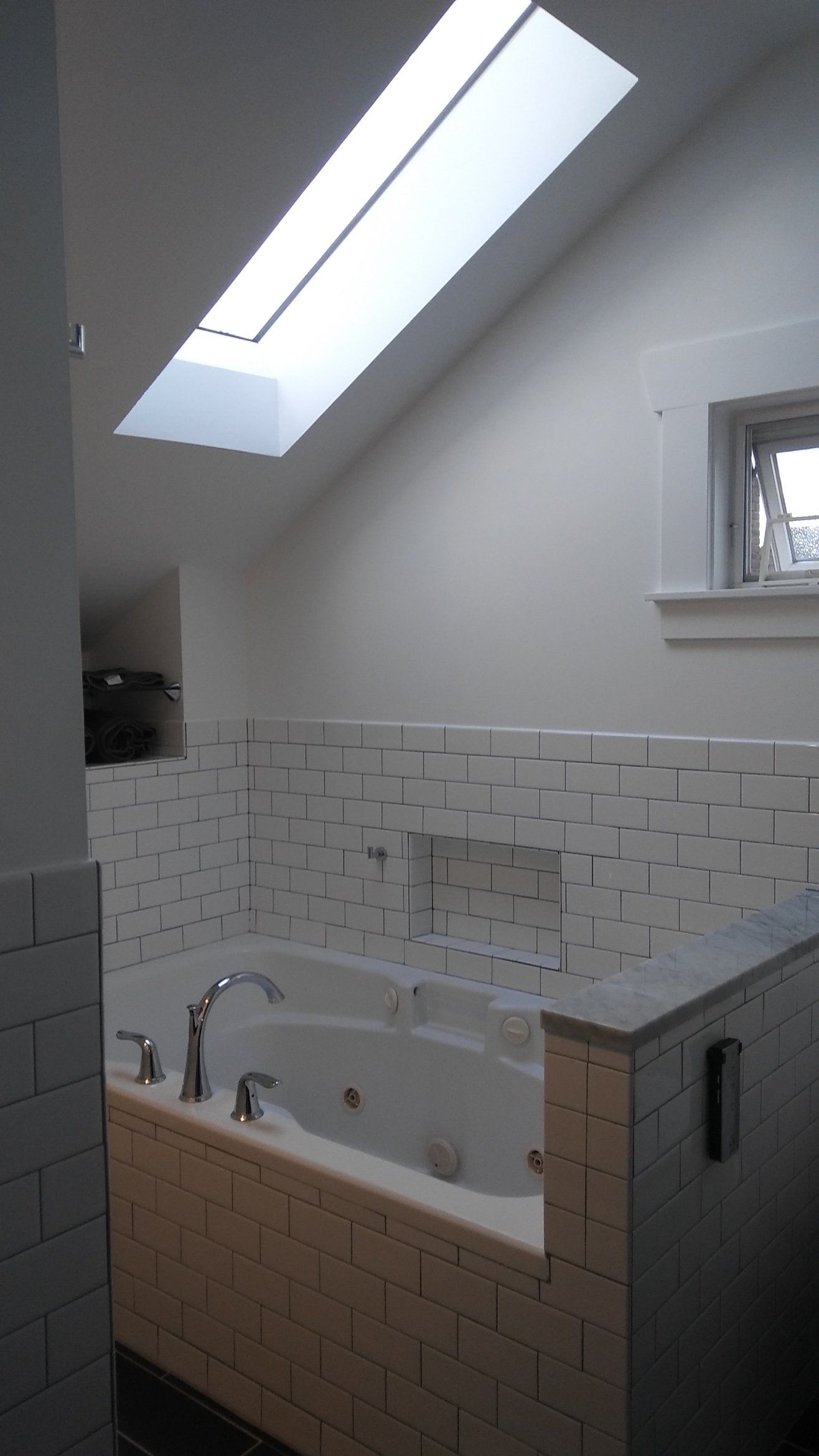 Bathroom with a white bathtub, tiled walls, skylight, and a small window.
