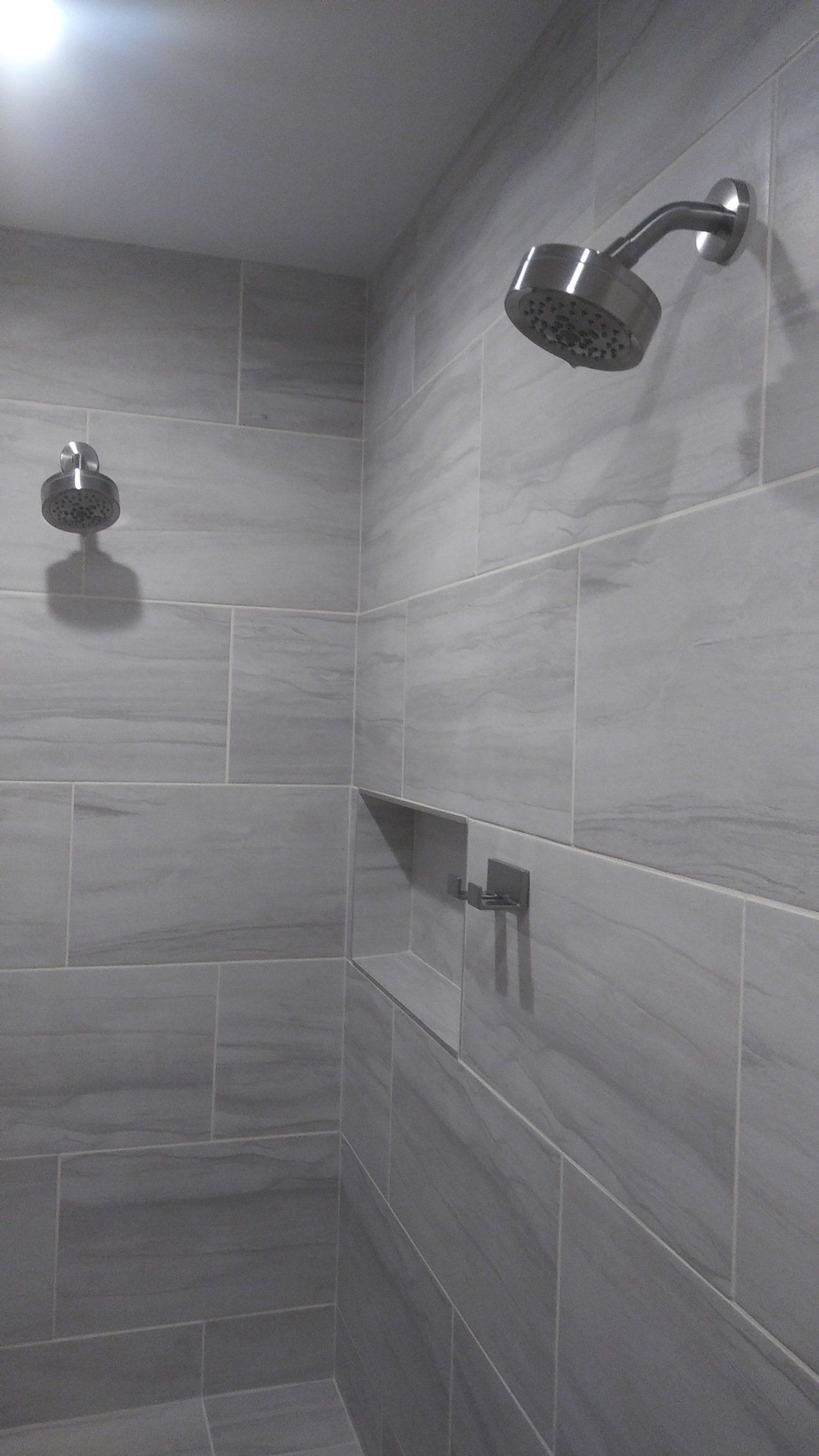Gray tiled shower with two showerheads and a built-in niche shelf