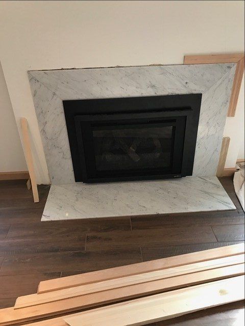 Modern black fireplace insert with white marble surround above dark wood flooring